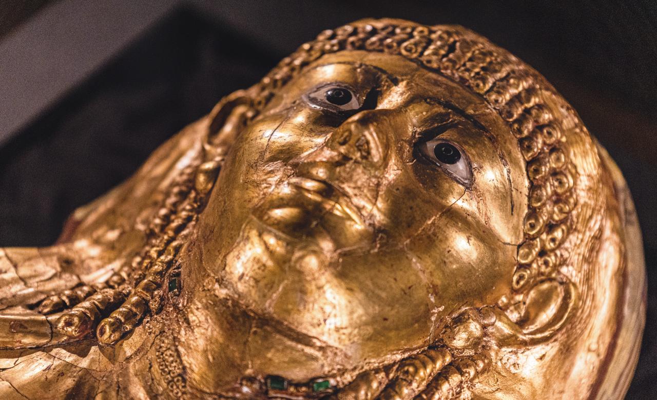 ABOVE This gilded mummy belonging to a woman called Isaious was discovered at Hawara in 1911. The mummy mask’s facial features and hairstyle are reminiscent of Ptolemaic ideals, while other elements of the cartonnage feature traditional Pharaonic iconography, reflecting the multiculturalism present in burial traditions in Egypt at the time.