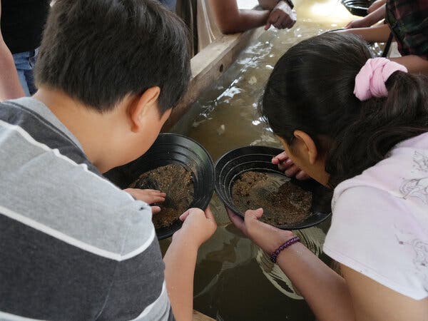 Two people hold what look like black bowls that contain dirt. 